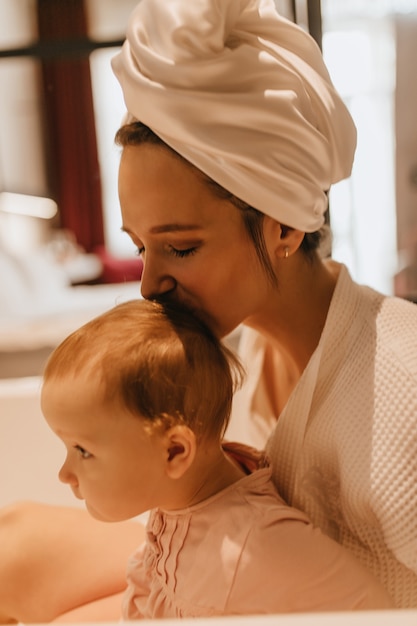 Photo gratuite portrait en gros plan de la belle femme en serviette sur la tête embrassant son bébé en couronne.