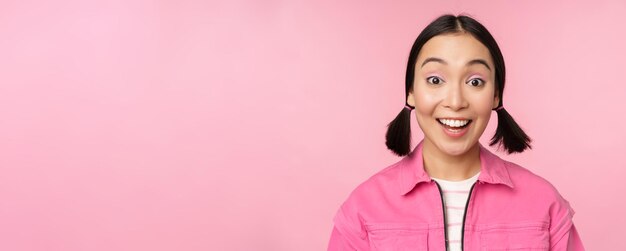 Portrait en gros plan d'une belle fille asiatique à la recherche d'enthousiasme et de sourire riant et souriant debout heureux sur fond rose