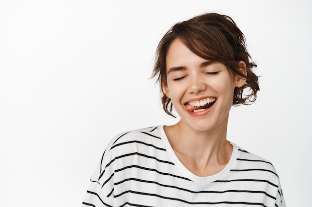 Portrait en gros plan d'une belle fille insouciante, femme riant et souriante, montrant la langue, le visage stupide, debout sur fond blanc.