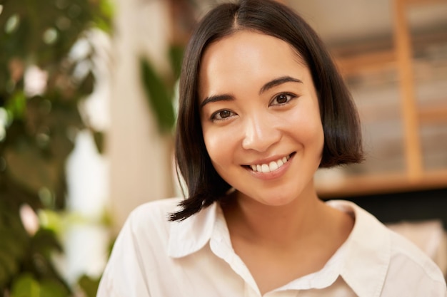 Photo gratuite portrait en gros plan d'une belle jeune femme asiatique romantique souriante et heureuse assise dans un confortable