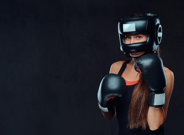 Portrait En Gros Plan D'une Boxeuse Portant Des Gants Et Un Casque De Protection Posant Dans Un Studio. Isolé Sur Un Fond Texturé Sombre.