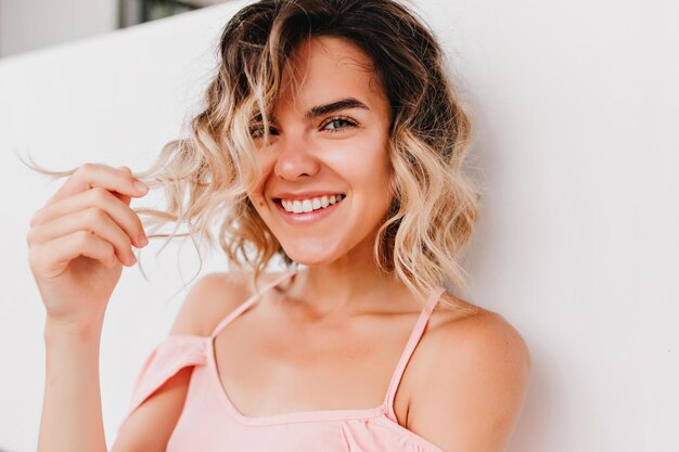 Portrait en gros plan d'une charmante fille riante jouant avec des cheveux ondulés Photo d'une femme bronzée intéressée avec un joli sourire