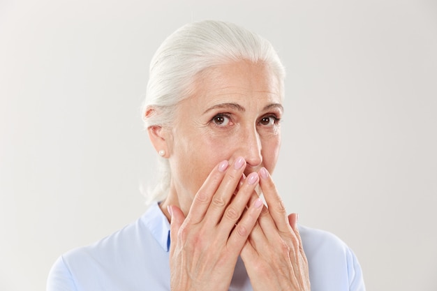 Portrait de gros plan de la charmante vieille dame, couvrant sa bouche avec les mains