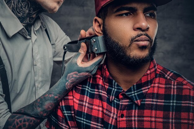 Portrait en gros plan de coupes de coiffeur masculin tatoué, barbe à un homme noir.