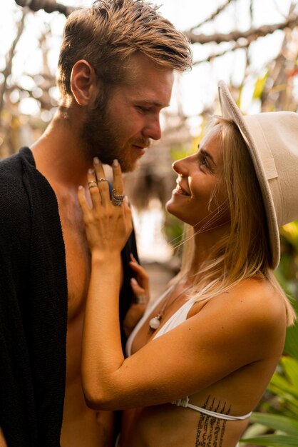 Portrait en gros plan d'un couple séduisant dans un jardin tropical Belle femme blonde en chapeau et tenue bohème étreignant avec son beau petit ami Moments romantiques d'été