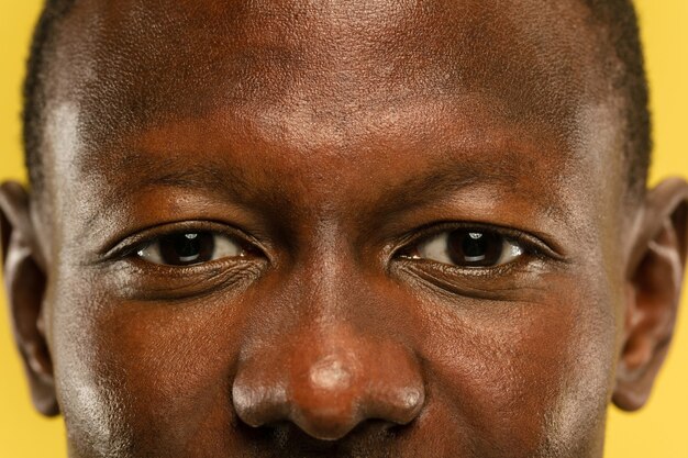 Portrait en gros plan du jeune homme afro-américain sur fond de studio jaune. Beau modèle masculin avec une peau bien entretenue. Concept d'émotions humaines, expression faciale, ventes, publicité. Yeux et joues.