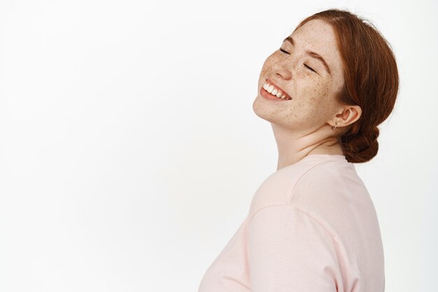 Portrait en gros plan du visage d'une femme rousse heureuse, yeux fermés et sourire insouciant, la beauté est dans le bonheur, rêvant de quelque chose de positif, de souvenirs agréables sur blanc.