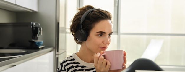 Photo gratuite portrait en gros plan d'une étudiante brune souriante qui boit son thé et écoute de la musique ou un livre électronique