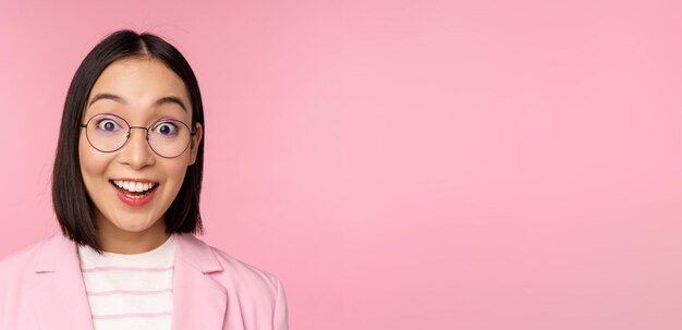 Portrait en gros plan d'une femme d'affaires asiatique dans des verres à la surprise de la réaction étonnée de la caméra debout en costume sur fond rose