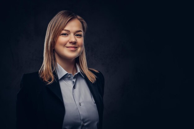 Portrait en gros plan d'une femme d'affaires blonde souriante habillée formellement. Isolé sur un fond texturé sombre.