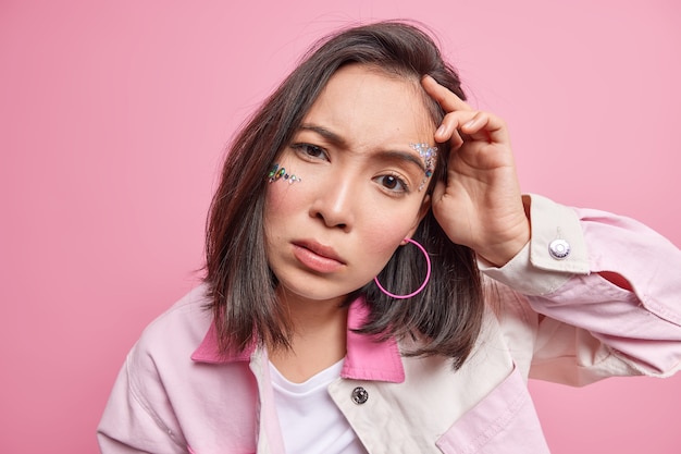 Portrait en gros plan d'une femme asiatique brune sérieuse et belle qui a l'air scrupuleusement le regard attentif lève les sourcils réagit à quelque chose de désagréable vêtu de vêtements élégants pose à l'intérieur