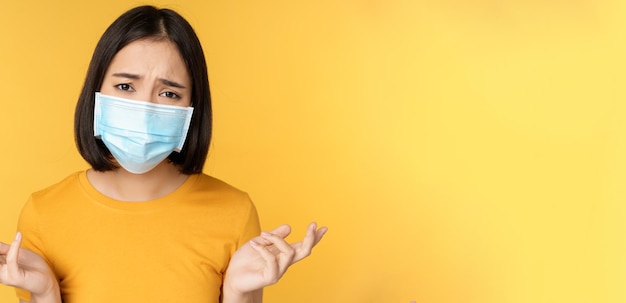 Portrait en gros plan d'une femme asiatique confuse portant un masque médical haussant les épaules et regardant perplexe