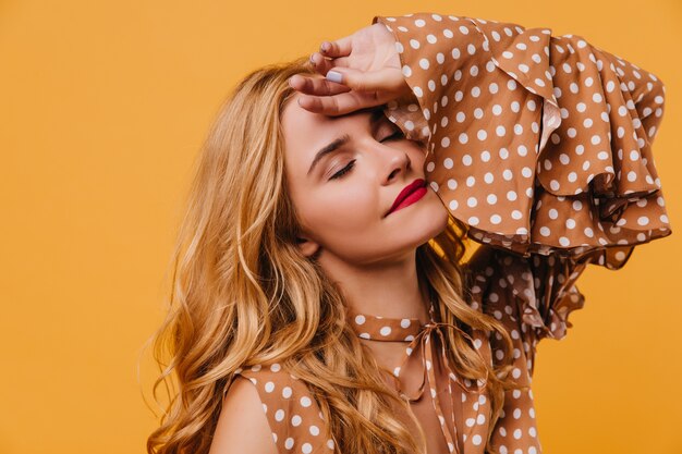 Portrait de gros plan d'une femme blonde détendue en robe magnifique. modèle féminin élégant debout sur un mur jaune.