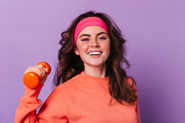 Portrait de gros plan de femme bouclée aux yeux verts en pull orange et bandeau de sport rose