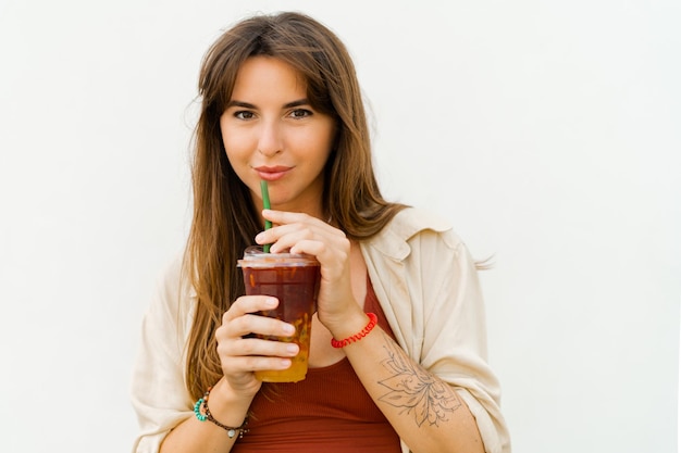 Portrait en gros plan d'une femme européenne souriante en tenue d'été élégante buvant de la limonade sucrée sur fond blanc