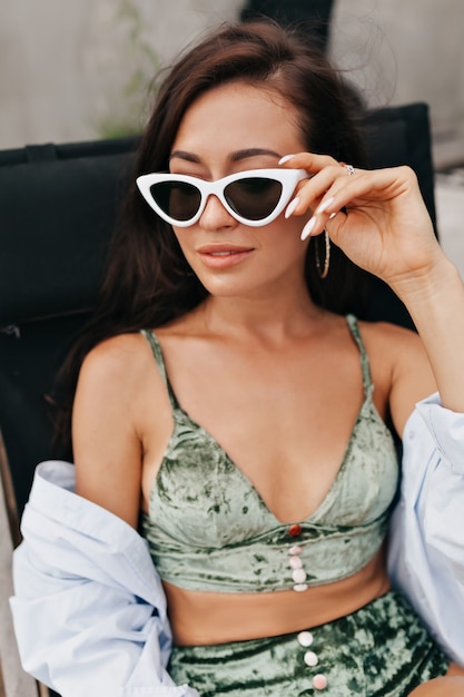 Photo gratuite portrait en gros plan d'une femme fantastique élégante dans des lunettes à la mode en lingerie de velours et chemise à la recherche de suite tout en vous relaxant sur une chaise longue