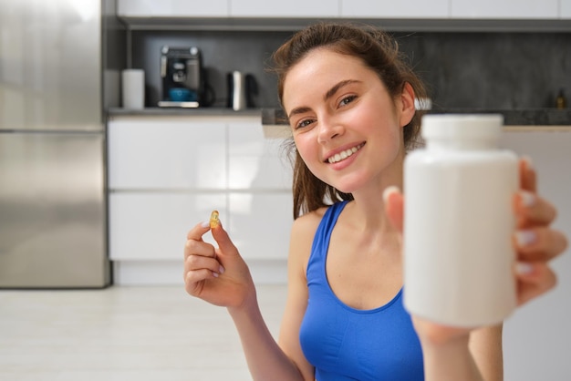 Portrait en gros plan d'une femme en forme, d'une fille qui s'entraîne à la maison, montrant une bouteille de vitamines diététiques