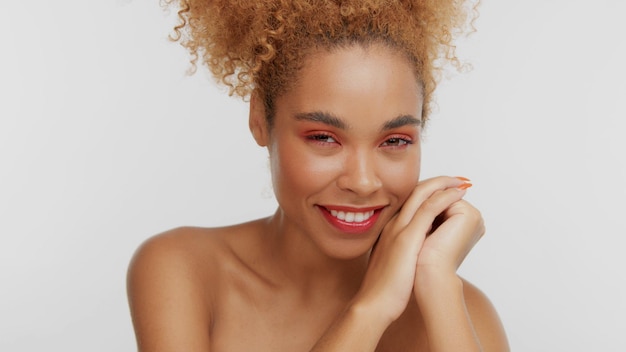 Portrait en gros plan d'une femme rase mixte avec du maquillage rouge en studio avec les mains sur le visage souriant à la caméra