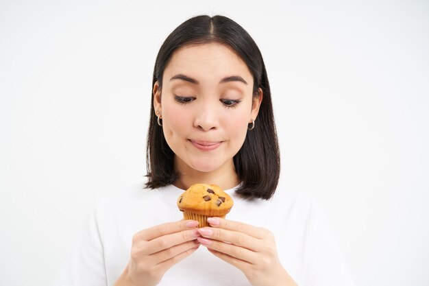 Portrait en gros plan d'une fille asiatique avec un délicieux cupcake qui a l'air pensif au dessert pendant son régime alimentaire