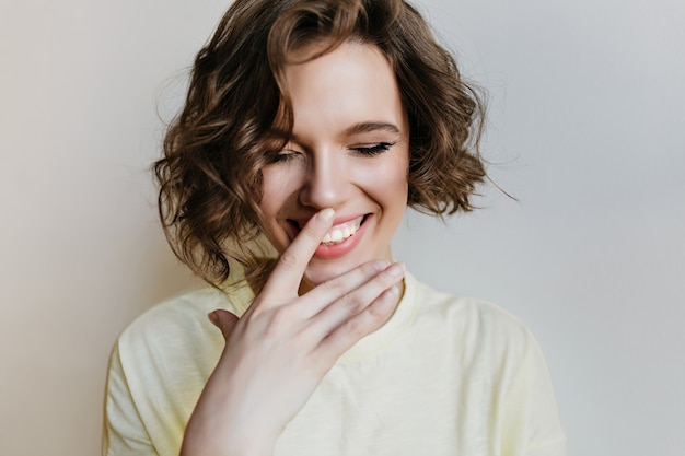 Portrait de gros plan d'une fille européenne heureuse avec une coupe de cheveux courte à la mode. heureuse femme brune posant avec un sourire timide et touchant son nez.