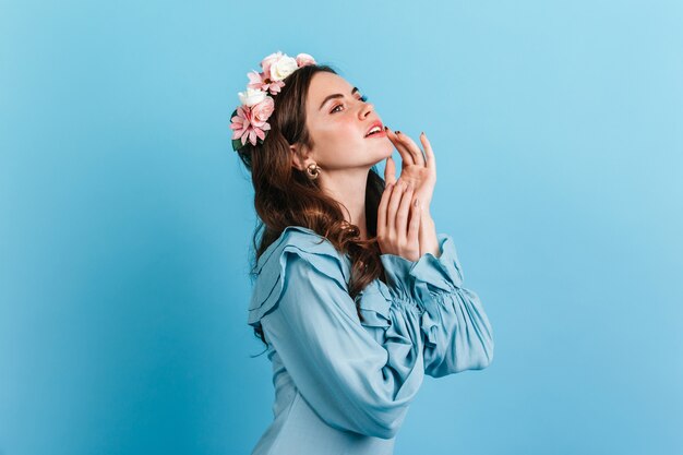 Portrait en gros plan d'une fille sensuelle en chemisier en soie à volants. Dame aux fleurs dans les cheveux touchant les lèvres.