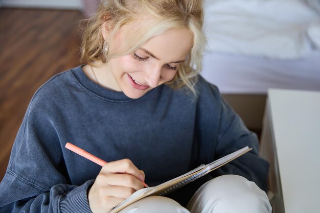 Portrait en gros plan d'une fille souriante écrivant dans un bloc-notes ajoute des notes à son journal souriante tout en faisant