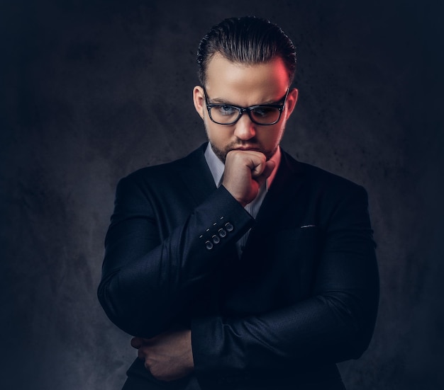 Photo gratuite portrait en gros plan d'un homme d'affaires élégant et réfléchi avec un visage sérieux dans un élégant costume formel et des lunettes. isolé sur un fond sombre.