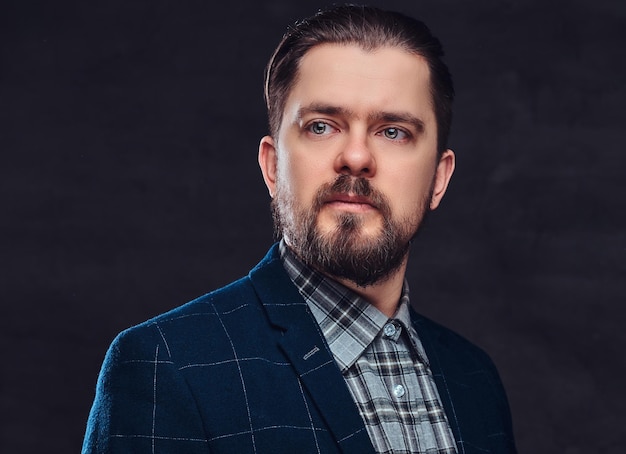 Portrait en gros plan d'un homme d'âge moyen avec barbe et coiffure vêtu d'un élégant costume bleu sur fond sombre texturé en studio.