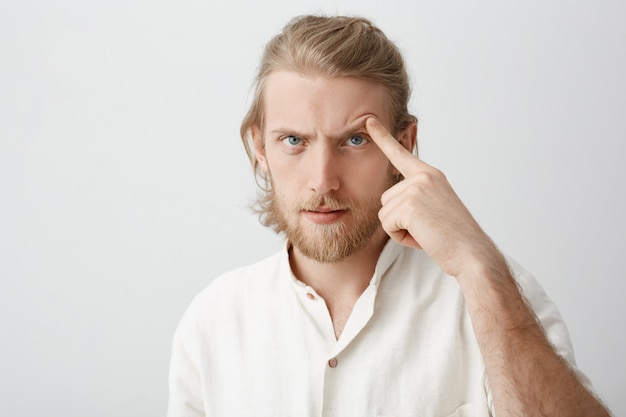 Portrait en gros plan d'un homme barbu attrayant sérieux aux cheveux blonds, soulevant le sourcil avec l'index comme s'il essayait de menacer ou d'effrayer quelqu'un