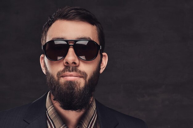 Portrait en gros plan d'un homme barbu portant un costume et des lunettes de soleil. Isolé sur un fond sombre.