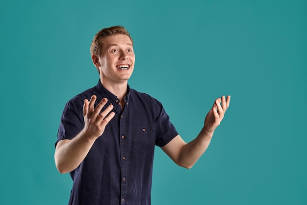 Portrait En Gros Plan D'un Jeune Beau Peson Au Gingembre Dans Un T-shirt Bleu Marine élégant Qui A L'air étonné Tout En Posant Sur Fond De Studio Bleu. Expressions Faciales Humaines. Concept D'émotions Sincères. Copier L'espace