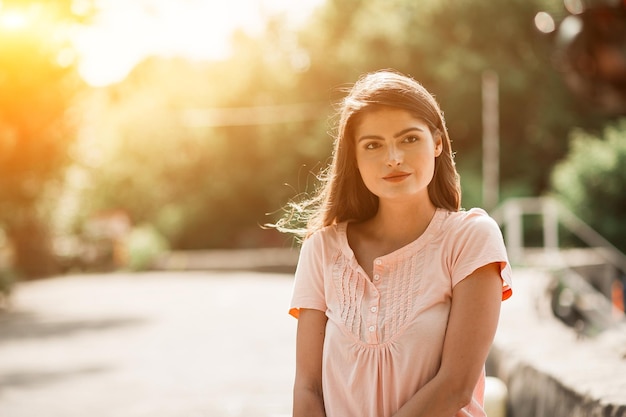 Portrait en gros plan d'une jeune brune sexy sur le côté droit de l'image. Le soleil brille sur ses cheveux mis sous son oreille. Elle regarde devant.