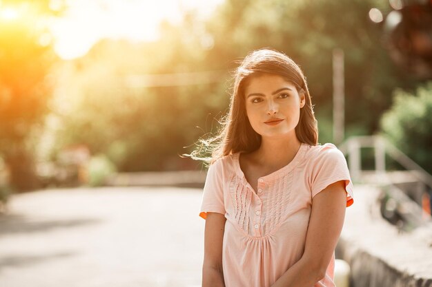 Portrait en gros plan d'une jeune brune sexy sur le côté droit de l'image. Le soleil brille sur ses cheveux mis sous son oreille. Elle regarde devant.