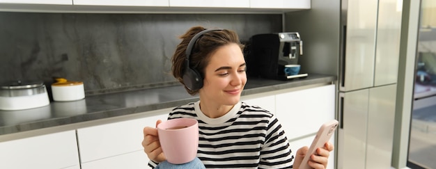 Portrait en gros plan d'une jeune étudiante buvant du thé et écoutant de la musique dans des écouteurs