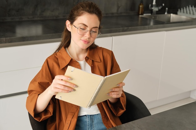 Portrait en gros plan d'une jeune étudiante dans la cuisine tenant un carnet de notes en train de réviser pour un examen à la maison