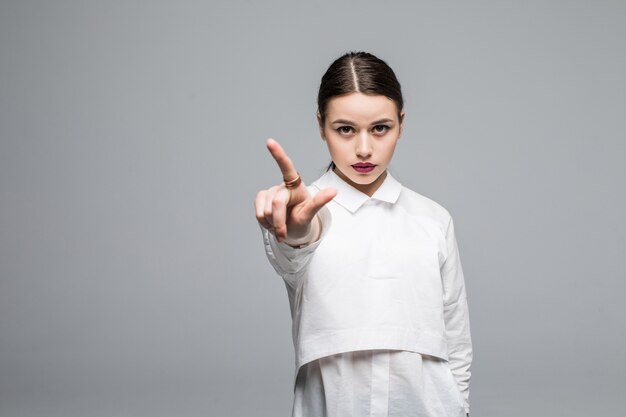 Portrait en gros plan d'une jeune femme d'affaires heureuse montrant quelque chose d'intéressant contre un mur blanc