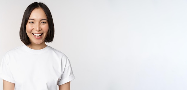 Portrait en gros plan d'une jeune femme asiatique regardant la caméra portant un t-shirt souriant et regardant un fond blanc heureux