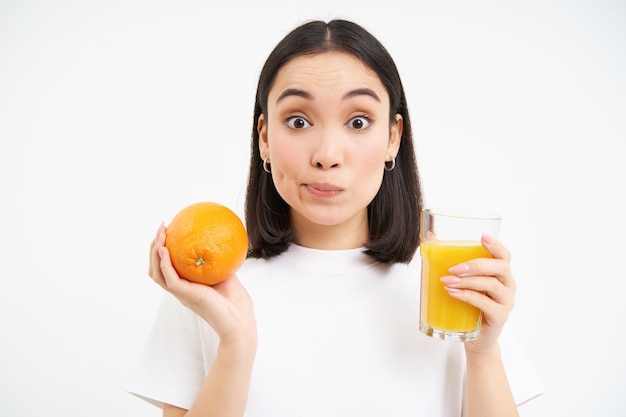 Photo gratuite portrait en gros plan d'une jeune fille brune regarde avec enthousiasme l'appareil photo contient des fruits et du jus d'orange en g