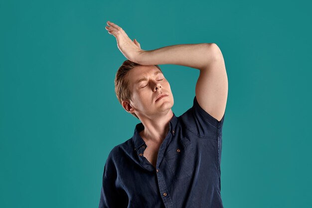 Portrait en gros plan d'un jeune homme au gingembre intelligent dans un t-shirt bleu marine élégant qui a l'air fatigué tout en posant sur fond de studio bleu. Expressions faciales humaines. Concept d'émotions sincères. Copiez l'espace.