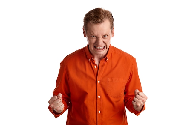 Portrait en gros plan d'un jeune homme élégant au gingembre dans une chemise orange élégante agissant comme s'il était hors de lui avec rage tout en posant isolé sur fond de studio blanc. Expressions faciales humaines. Sinc