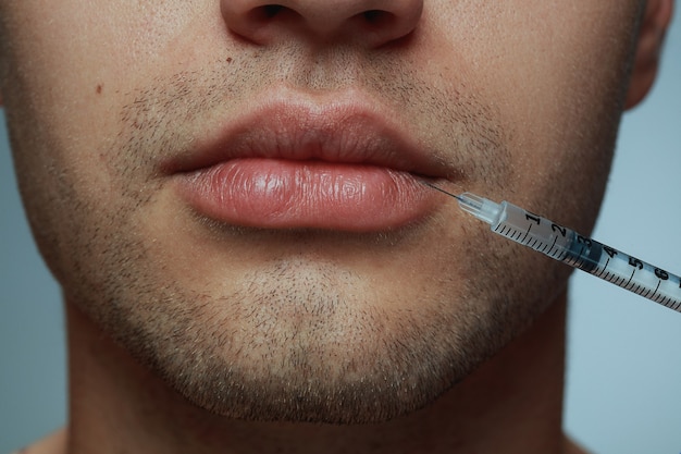 Portrait de gros plan de jeune homme isolé sur fond gris. Procédure de chirurgie de remplissage.