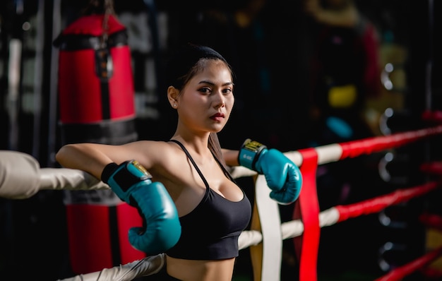 Portrait en gros plan jeune jolie femme en gant de boxe debout sur toile après entraînement avec fatigue, entraînement en salle de fitness,