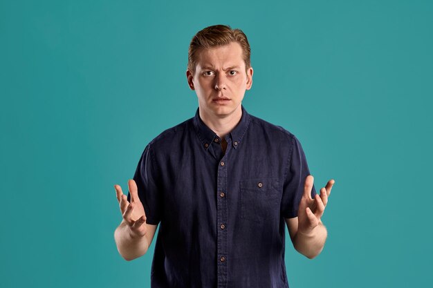 Portrait en gros plan d'un jeune peson attrayant au gingembre dans un t-shirt bleu marine élégant, choqué par quelque chose tout en posant sur fond de studio bleu. Expressions faciales humaines. Concept d'émotions sincères