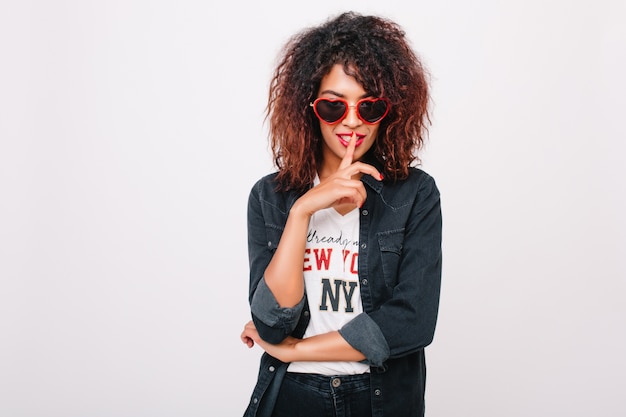 Portrait de gros plan de jolie fille avec une peau marron clair brillante isolée. Photo intérieure d'une élégante jeune femme noire à lunettes de soleil porte des vêtements en denim à la mode.