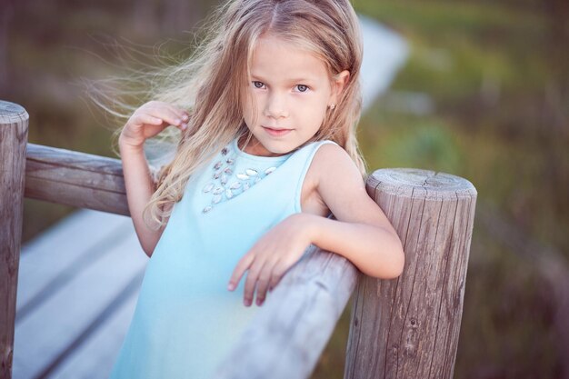 Portrait en gros plan d'une jolie petite fille, debout à l'extérieur tout en s'appuyant sur une clôture en bois.