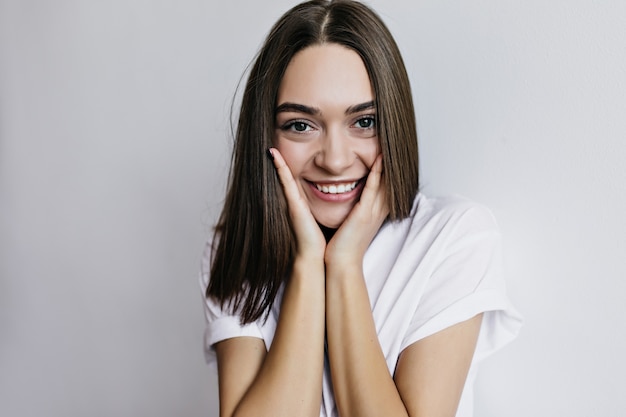 Portrait en gros plan d'une magnifique fille aux grands yeux bruns. Plan intérieur d'une femme romantique légèrement bronzée posant avec un sourire sincère.