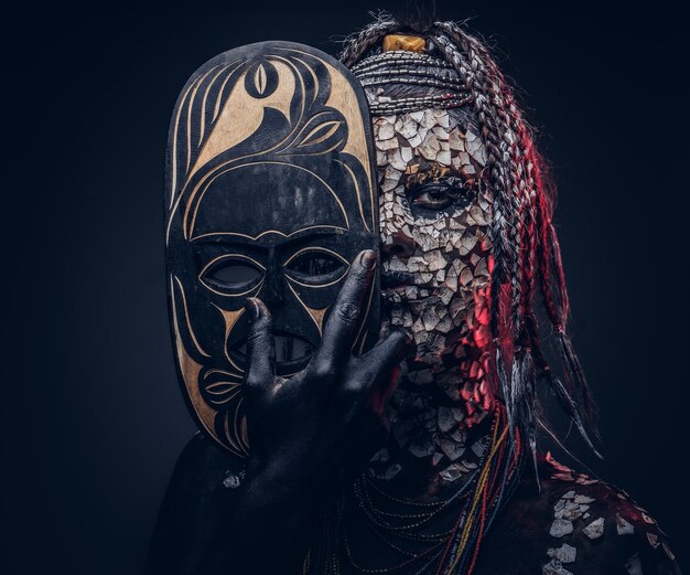 Portrait en gros plan d'une sorcière de la tribu africaine indigène, vêtue d'un costume traditionnel. Notion de maquillage. Isolé sur un fond sombre.