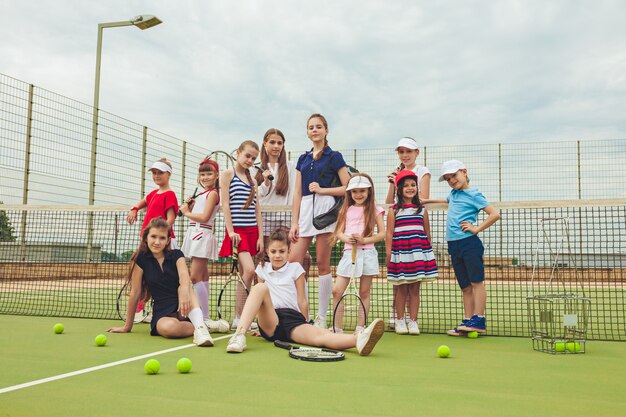Portrait d'un groupe de filles et de garçons en tant que joueurs de tennis tenant des raquettes de tennis contre l'herbe verte de la cour extérieure.