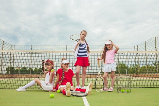 Portrait de groupe de filles en tant que joueurs de tennis tenant des raquettes de tennis contre l'herbe verte du terrain extérieur.