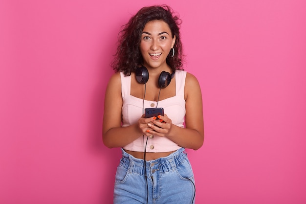 Portrait de l'heureuse belle jeune femme tenant le téléphone à la main et souriant, portant des vêtements décontractés